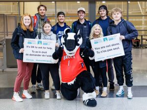 A group of Brock student-athletes pose with the University’s mascot, Boomer the Badger. Two students hold signs that read “It’s OK to ask for help” and “You are not alone.”