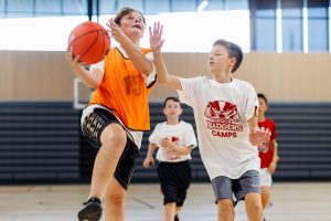 Two boys play basketball inside during a summer camp.