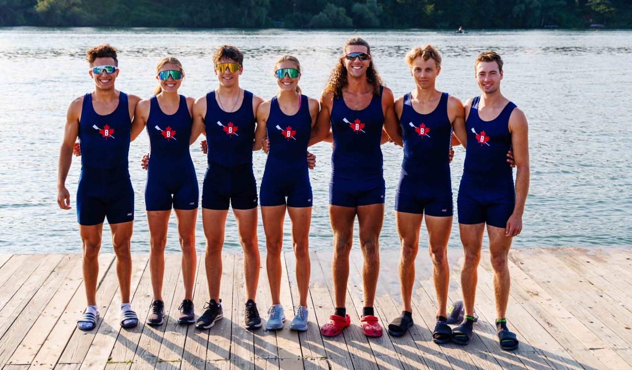 A group of male and female Brock University rowers stand on a dock surrounded by water on Henley Island.