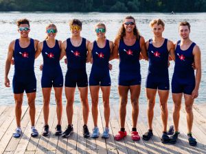 A group of male and female Brock University rowers stand on a dock surrounded by water on Henley Island.