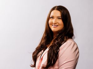 A young woman in a pink blazer poses for a portrait against a light backdrop.