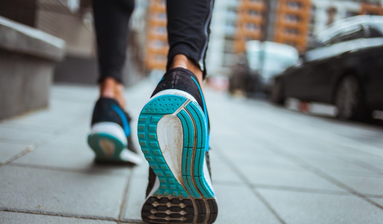 Close-up of running shoes as someone walks on a sidewalk.