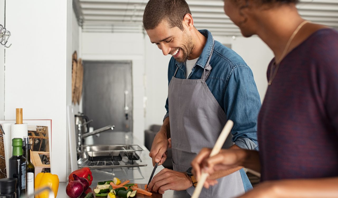 A happy young couple chops vegetables and cooks in a kitchen.