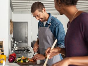 A happy young couple chops vegetables and cooks in a kitchen.