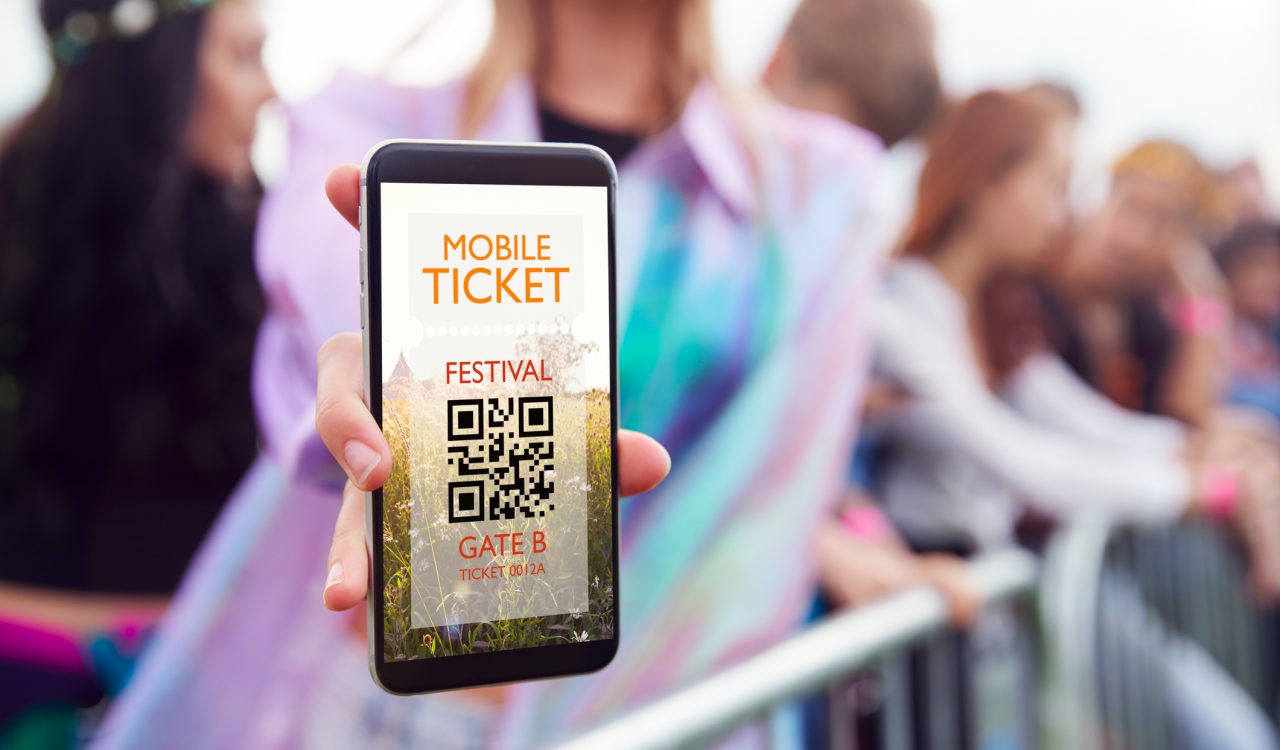 Close-up of a woman holding a smartphone with a mobile ticket on it at a music festival.