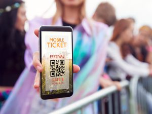 Close-up of a woman holding a smartphone with a mobile ticket on it at a music festival.