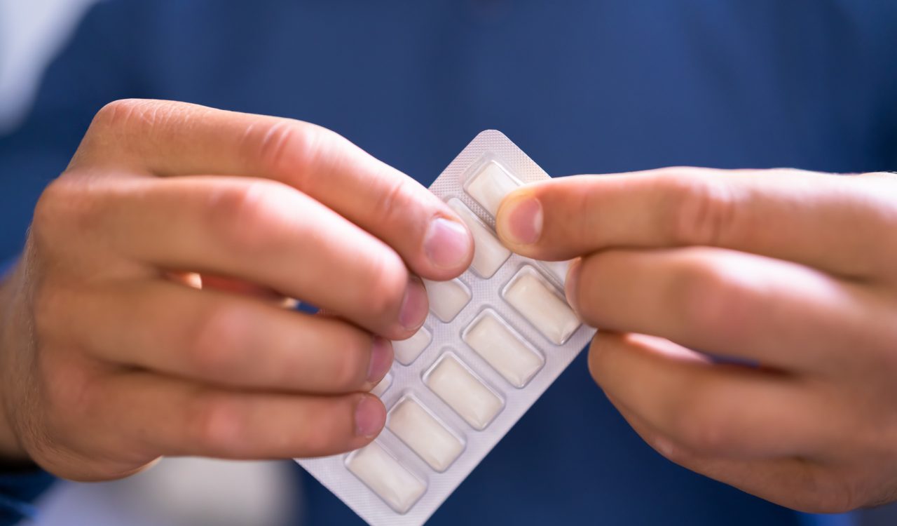 Close-up of two hands gripping a blister-pack of nicotine gum.