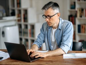 An older adult man works on a laptop in a living room.