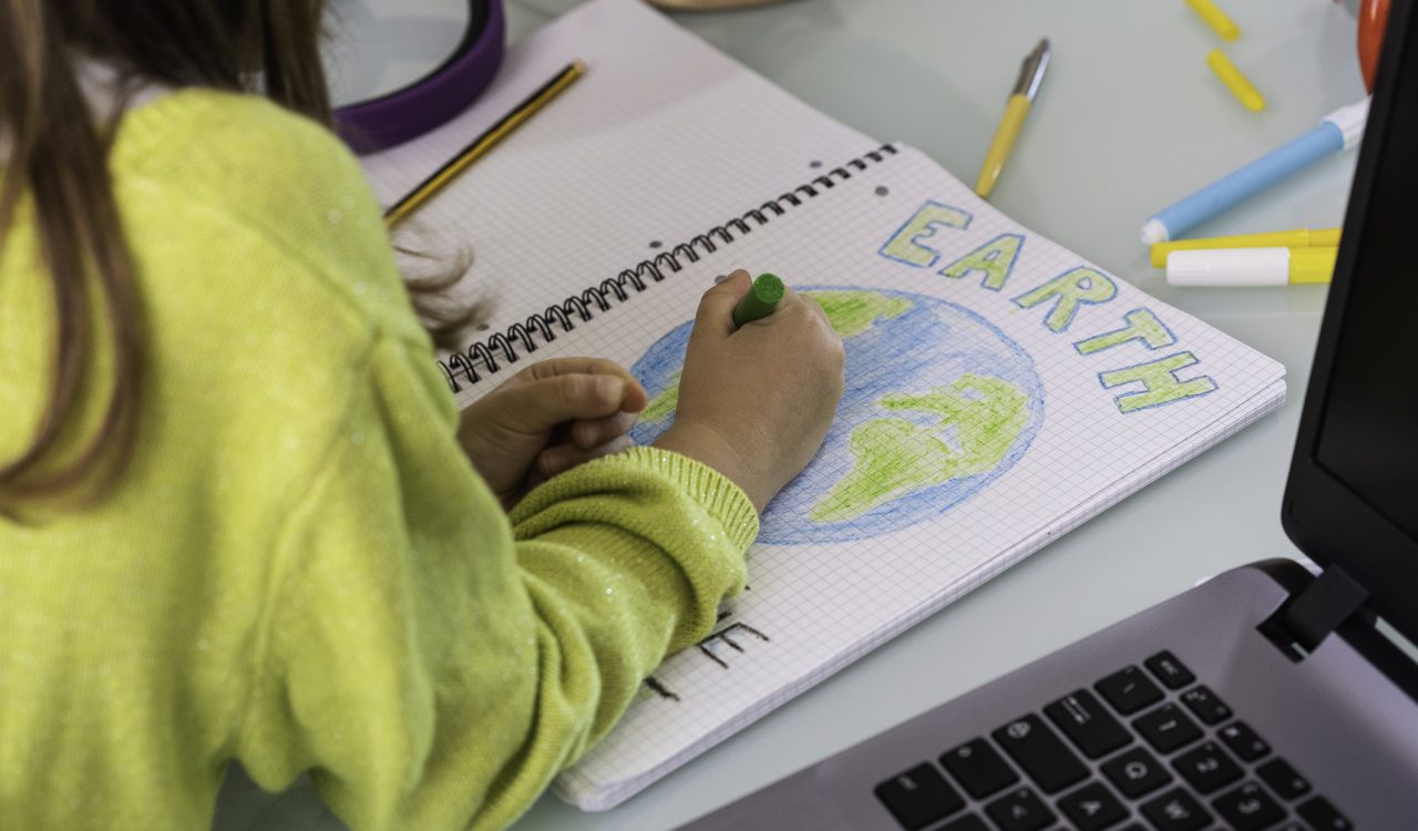 Close-up view over the shoulder of a child who is colouring in a drawing of the Earth.