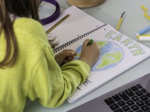 Close-up view over the shoulder of a child who is colouring in a drawing of the Earth.