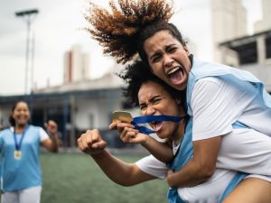 Female soccer players hold up medals and hug on a field.