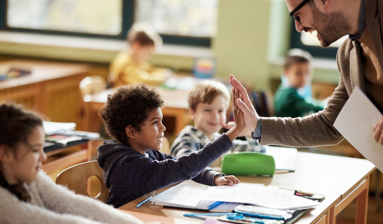 A male teacher gives a young child a high five.