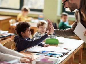 A male teacher gives a young child a high five.