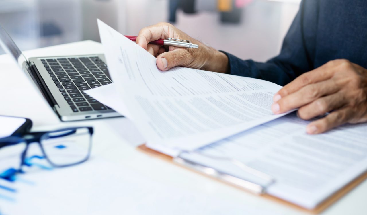 Close-up view of hands holding a document beside a laptop.