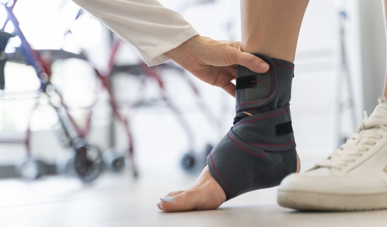 Close-up of a hand adjusting an ankle brace around a patient's foot in a medical setting.