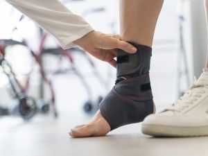 Close-up of a hand adjusting an ankle brace around a patient's foot in a medical setting.