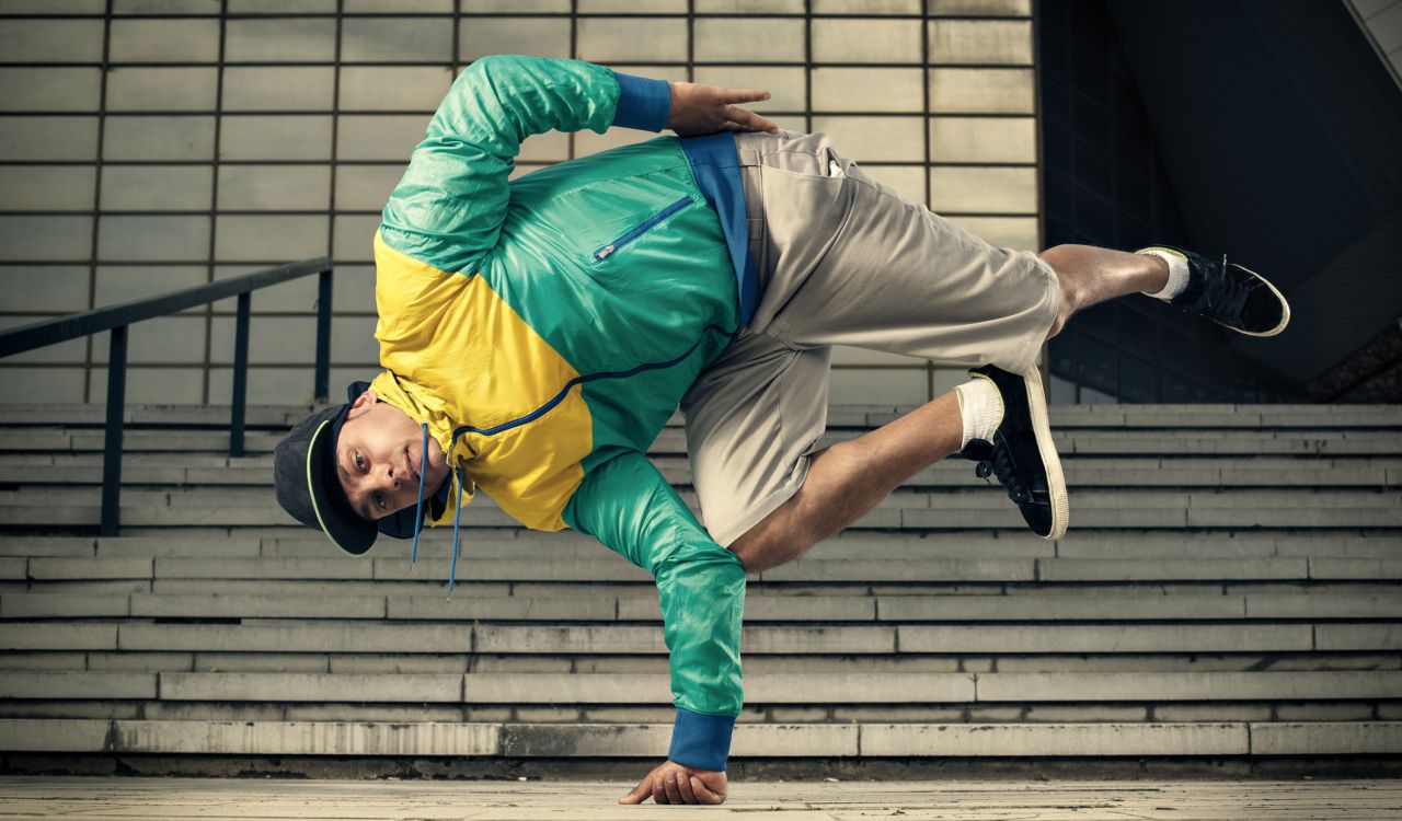 A young man balances himself on the knuckles of his one hand with the rest of his body in the air, bend at the waist.