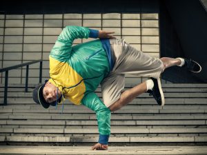 A young man balances himself on the knuckles of his one hand with the rest of his body in the air, bend at the waist.