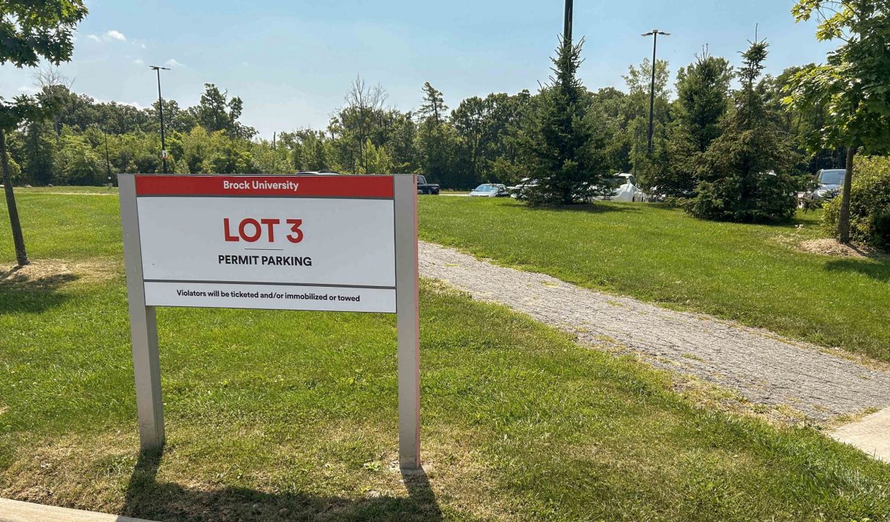 A sign reading “Lot 3” stands in the grass at the edge of one of a parking lot.