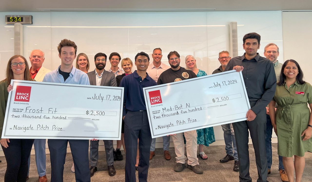 A large group of people poses with two giant cheques.