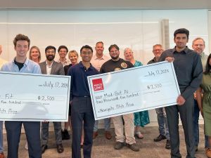 A large group of people poses with two giant cheques.