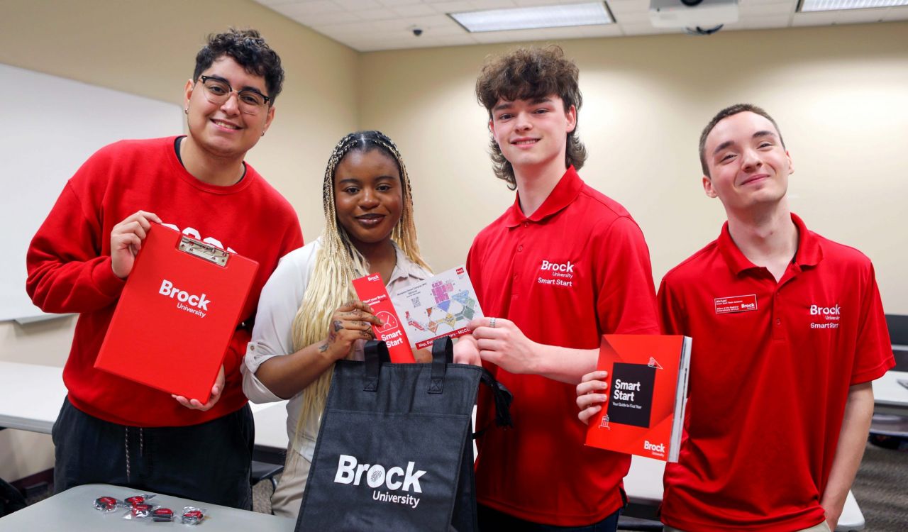 Four Brock University Smart Start team members stand at a table in a classroom while placing swag items into bags.