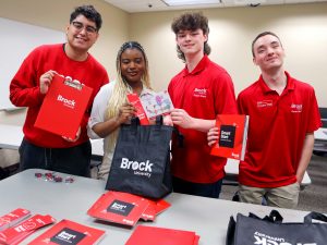 Four Brock University Smart Start team members stand at a table in a classroom while placing swag items into bags.