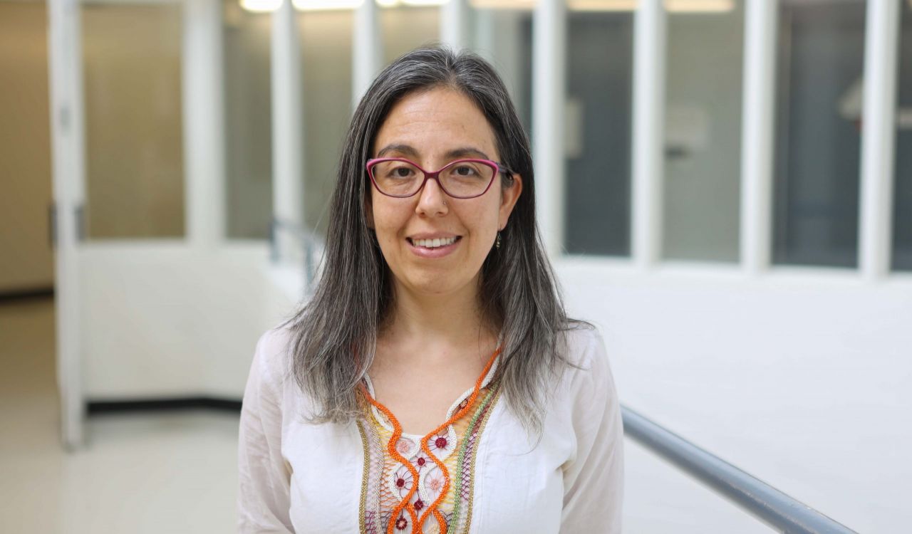 Head and shoulders photo of Paula Duarte-Guterman smiling into the camera, with a blurred-out hallway/laboratory in the background.