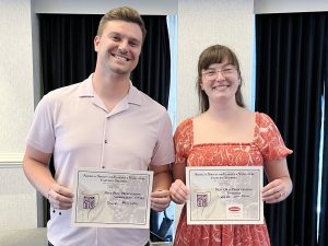 Two people standing next to each other holding first-place certificates.