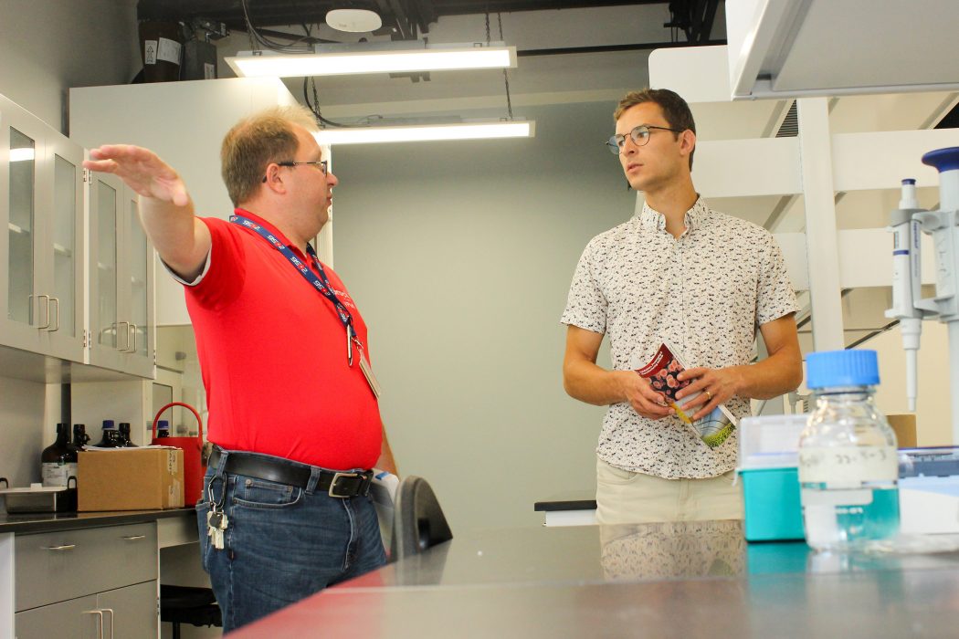 Two men stand in conversation in a scientific laboratory.