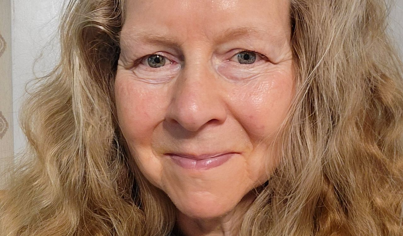 A portrait photo of Brock Professor Elizabeth Sauer shows her from the shoulders up, smiling at the camera. She has long, blond hair and a dark green shirt.