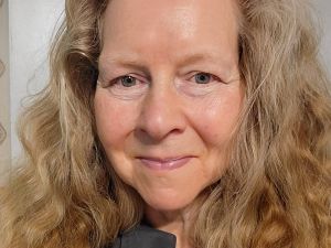 A portrait photo of Brock Professor Elizabeth Sauer shows her from the shoulders up, smiling at the camera. She has long, blond hair and a dark green shirt.