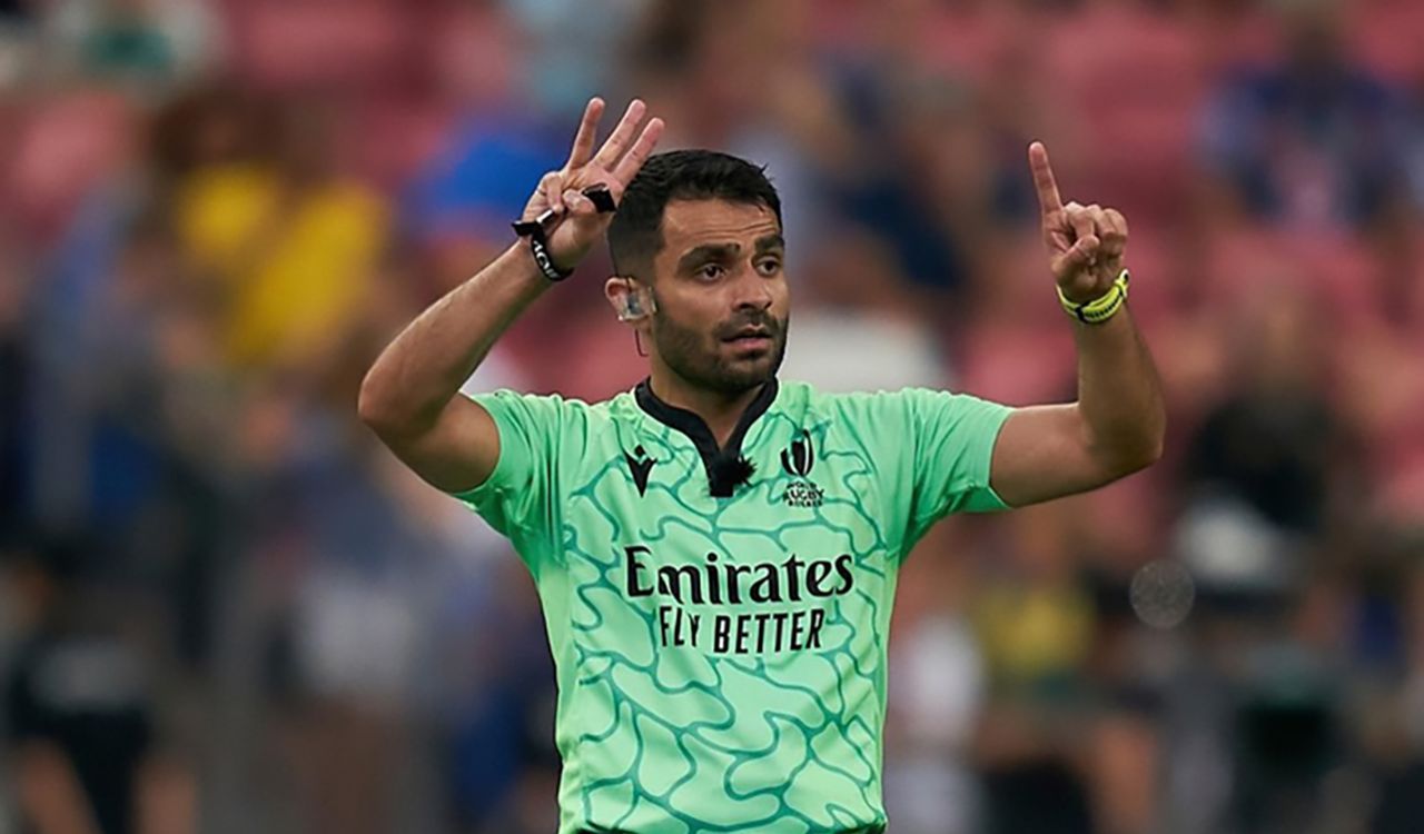 A referee completes a sign with his hands while officiating the sport of rugby outdoors.