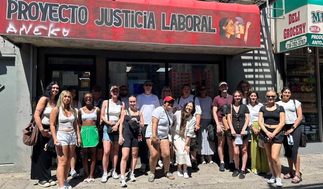 University students pose on the sidewalk under the awning of the Proyecto Justica Laboral (Workers’ Justice Project) in Brooklyn, New York.