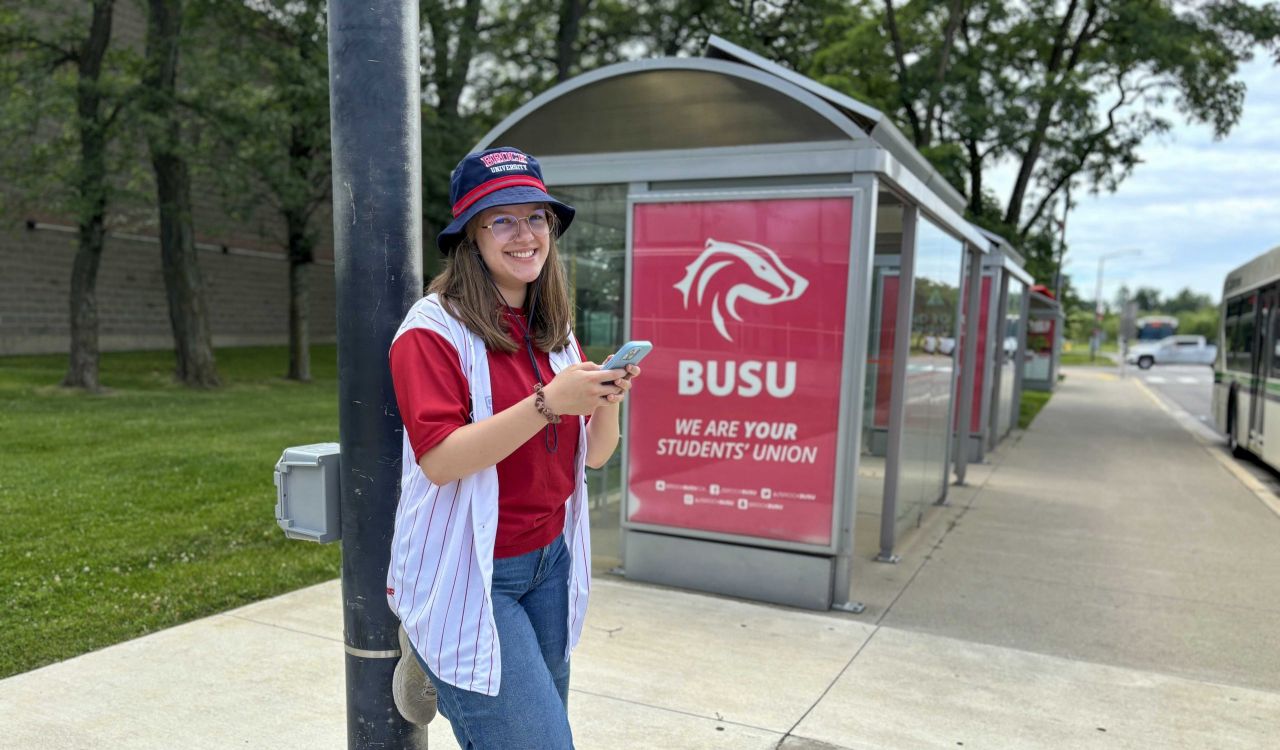 A young woman stands beside a bus shelter.