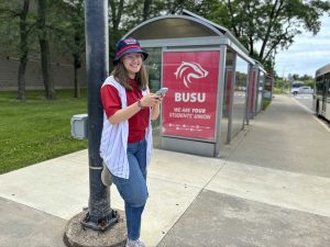 A young woman stands beside a bus shelter.