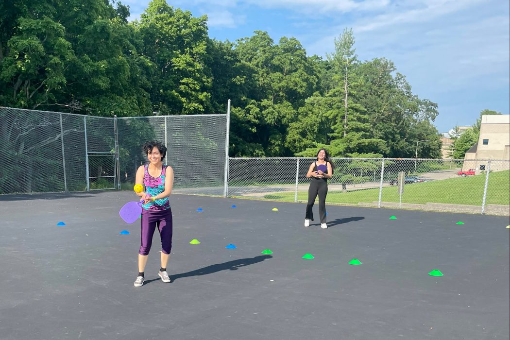 Two young women play pickleball outside on a sunny day.