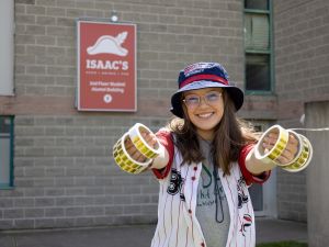 A young woman stands outside a grey building holding up rolls of gold stickers for a photo.