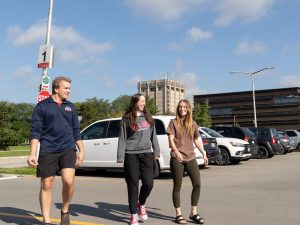 Three students walk across Lot 1 with the Schmon Tower in the background.