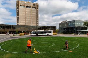 Two men use white paint to sketch out a giant number 60 on the front green lawn of Brock University’s main campus.