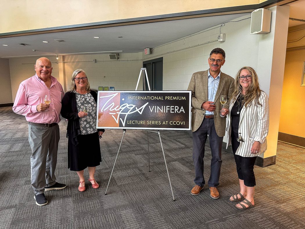 Four people stand around a sign for the Triggs International Premium Vinifera Lecture Series.