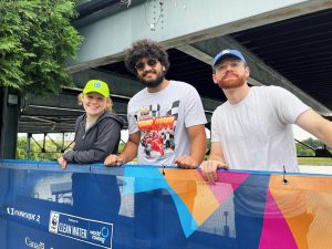 Three Brock University students lean on large signage for the World Rowing Championships.