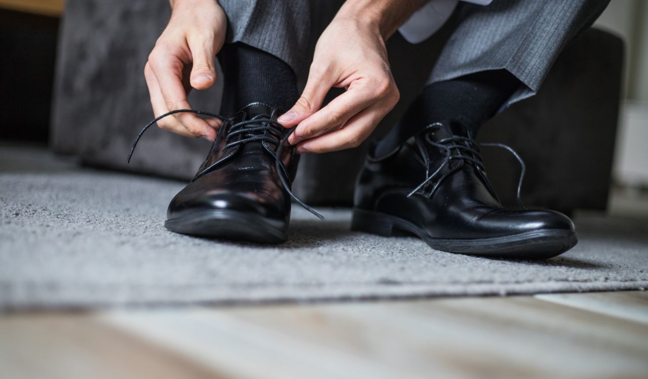 Alt text: Image of man’s hands tying the shoelaces of black, leather dress shoes.