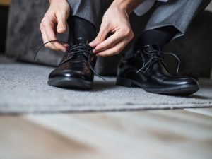 Alt text: Image of man’s hands tying the shoelaces of black, leather dress shoes.