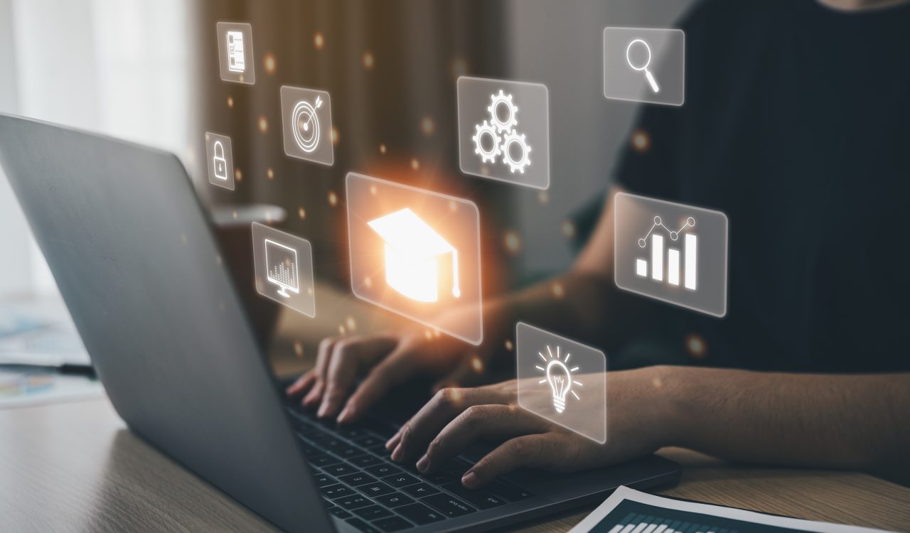 Close-up of hands typing on a laptop with glowing business and education icons hovering above it.