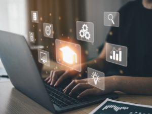 Close-up of hands typing on a laptop with glowing business and education icons hovering above it.