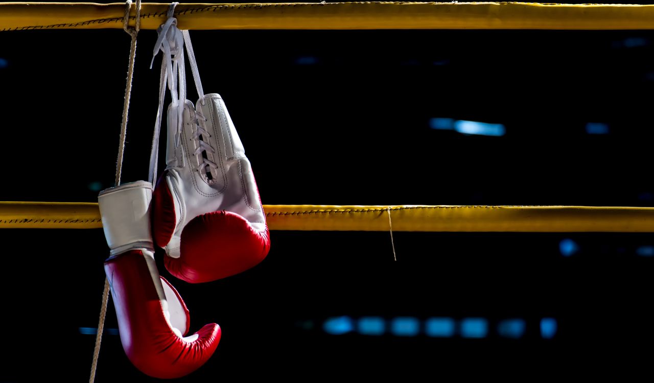 A pair of boxing gloves hang over the ropes of a boxing ring.