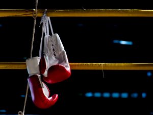 A pair of boxing gloves hang over the ropes of a boxing ring.