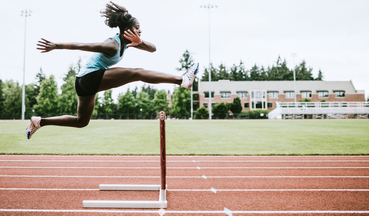 A female athlete jumps over a hurdle on a running track.