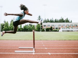 A female athlete jumps over a hurdle on a running track.